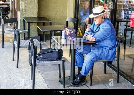 West Palm Beach Florida Clematis Street Senior Mann männlich blau Anzug sitzen Fast-Food-Restaurant Tisch mit kostenlosem WiFi Laptop-Makler Broker Stockfoto