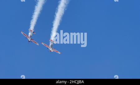 Thiene Italien 16. OKTOBER 2021 zwei Propellerflugzeuge machen eine Schleife mit weißem Rauch am blauen Himmel mit Kopierraum. Yakovlev Yak-52 von YAK Italia Stockfoto
