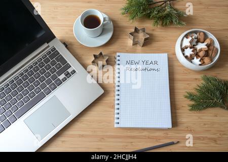Neujahrsvorsätze auf einem Spiralnotizbuch auf einem Desktop mit Laptop, Kaffee, Keksen und Tannenzweigen, Kopierplatz, Draufsicht von oben, Auswahl Stockfoto