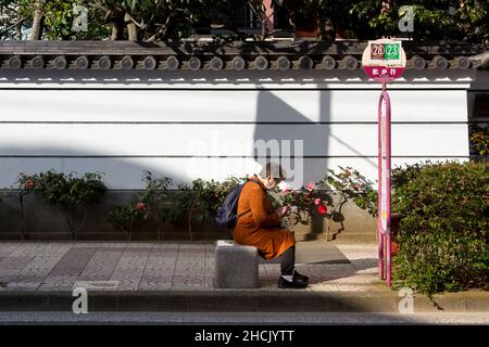 Eine ältere Japanerin sitzt an einer Bushaltestelle in Kappabashi, in der Nähe von Ueno Tokyo, Japan. Stockfoto