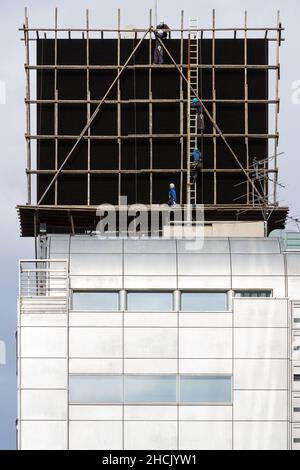 Arbeiter, die auf einem Werbebrett auf einem Gebäude in Roppongi, Tokio, Japan, um ein Gerüst herumlaufen. Stockfoto