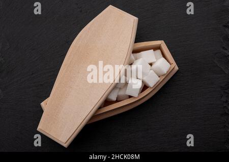 Diabetes-Krankheit, Insulinresistenz und zugesetzten Zucker töten Sie Konzept mit Sarg gefüllt mit Zuckerwürfeln isoliert auf dunkelschwarzem Hintergrund Stockfoto