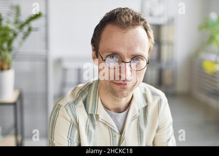 Horizontale Nahaufnahme aus einem hohen Winkel des kaukasischen Mannes mit Brille, der im modernen Büro am Schreibtisch sitzt und die Kamera anschaut Stockfoto