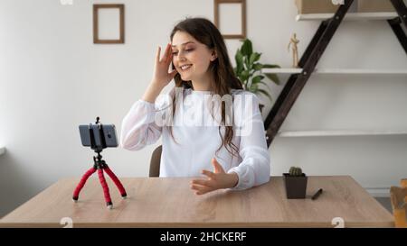 Eine emotionale, tausendjährige kaukasische Bloggerin, die an einem Schreibtisch in einem Büro sitzt, streamt live über den Blog. Kopfschmerzen eines Mädchens, das sich unterhielt Stockfoto