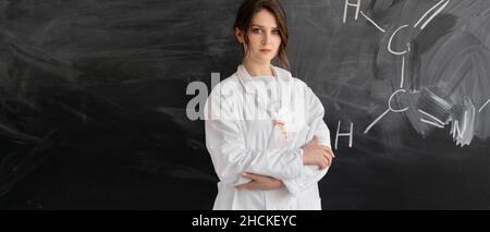 Chemielehrerin oder Schülerin steht vor dem Hintergrund der Tafel mit einer chemischen Formel. Konzept zurück in die Schule. Stockfoto