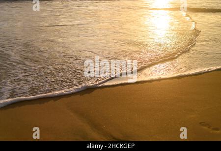 Das Licht des Sonnenuntergangs scheint auf den Wellen des Ozeans. Tropischer Sandstrand Sonnenuntergang Reflexion. Stockfoto