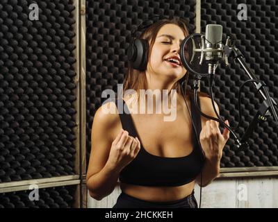 Schöne Frau, die in einem professionellen Aufnahmestudio in ein großes Membranmikrofon singt. Stockfoto