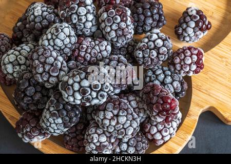 Gefrorene Brombeeren sehen frostig aus und sind auf Holzteller zu sehen Stockfoto