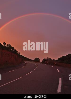 Schöner Blick auf die kurvenreiche Straße D559 an der mittelmeerküste in der Nähe von Saint-Raphael, an der französischen Riviera nach Sonnenuntergang mit atemberaubendem farbenfrohem Regenbogen. Stockfoto