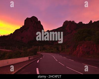 Blick auf die zerklüfteten Felsen von Cap Roux an der mittelmeerküste mit gewundener Straße D559 nach Sonnenuntergang mit farbenfrohem, dramatischem Himmel in der Nähe von Saint-Raphael, Frankreich. Stockfoto