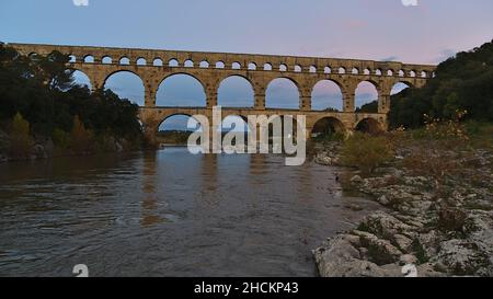 Schöner Blick auf das antike römische Aquädukt Pont du Gard, das nach Sonnenuntergang den Fluss Gardon überquert, in der Nähe von Vers-Pont-du-Gard, Oczitanie, Frankreich. Stockfoto