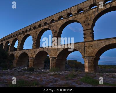 Schöner Blick auf das antike römische Aquädukt Pont du Gard mit Steinbögen, die den Fluss Gardon am Abend in der Nähe von Vers-Pont-du-Gard, Ockitanie, Frankreich, durchqueren. Stockfoto