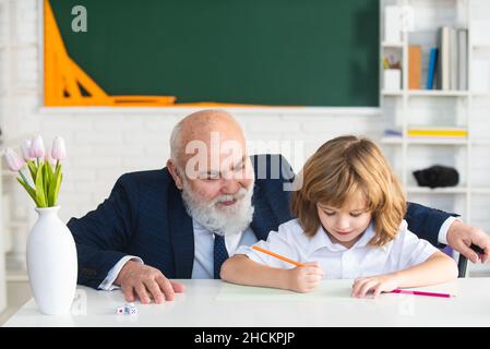 Oberlehrer oder Großvater und Schüler im Klassenzimmer der Schule. Grundschüler lesen und schreiben mit Lehrer im Klassenzimmer. Stockfoto