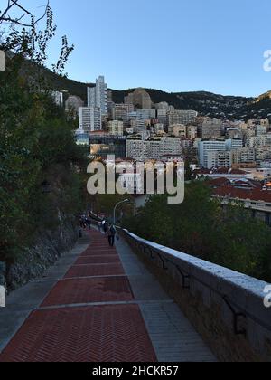 Am Abend steigt man auf den Weg nach Monaco-Ville in der Innenstadt von Monaco an der französischen Riviera mit Hochhäusern im Hintergrund. Stockfoto