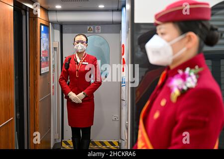 (211230) -- PEKING, 30. Dezember 2021 (Xinhua) -- Crew-Mitglieder warten auf Passagiere in einem Zug des Hochgeschwindigkeitszuges Peking-Zhangjiakou am Pekinger Nordbahnhof in Peking, der Hauptstadt von China, am 30. Dezember 2021. Die Hochgeschwindigkeitsbahn, die Peking und Zhangjiakou in der nordchinesischen Provinz Hebei verbindet, wurde am 30. Dezember 2019 in Betrieb genommen. (Foto von Fang Xin/Xinhua) Stockfoto