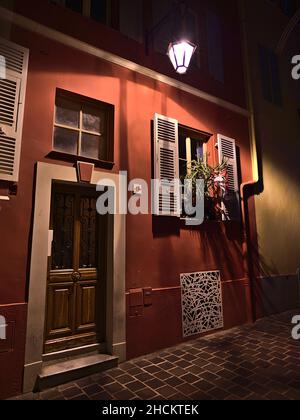 Vorderansicht des alten Gebäudes im historischen Zentrum von Monaco (Monaco-Ville) an der französischen Riviera in einer engen Gasse mit Holztür und Beleuchtung. Stockfoto