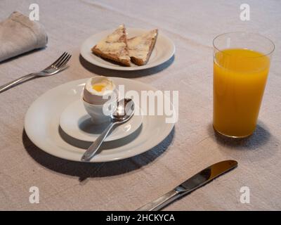 Frühstückstisch mit gekochtem Ei und einem Glas Orangensaft und gebuttertem Toast Stockfoto