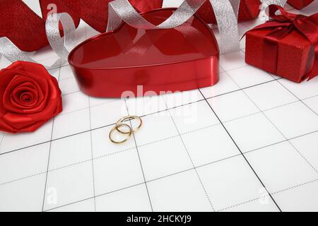 Valentinstag- und Hochzeitskonzept, goldene Eheringe, rote herzförmige Geschenkbox, glänzende Schleife und Rosenblume auf weißem Hintergrund mit Copy-Verpackung Stockfoto