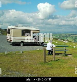 Der Fahrer des Brecon Beacons National Park reist in einem Layby VW Wohnmobil mit Blick auf die sanfte Hügellandschaft von South Wales UK an einem Picknick-Tisch Stockfoto