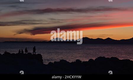 Atemberaubender Sonnenuntergang in der Nähe von Antibes, an der französischen Riviera, Frankreich an der mittelmeerküste mit Silhouetten von Fischern, die auf Felsen und farbenprächtiger Himmel stehen. Stockfoto