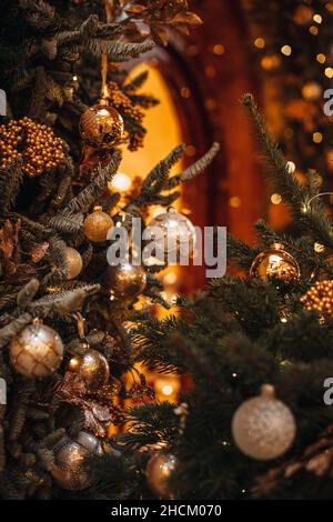 Grüner Zweig des Weihnachtsbaums mit einem goldenen magischen Girlanden Licht und Weihnachtskugeln geschmückt. Neujahrskomposition in einem festlichen Interieur Stockfoto