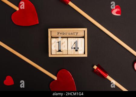 Draufsicht auf Holzkalender mit 14. februar in der Nähe herzförmiger Lutscher auf Schwarz Stockfoto