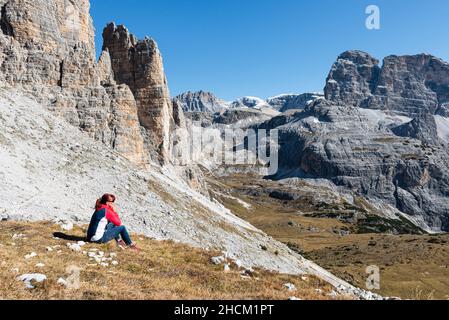 Frau sitzt im Herbst auf einer Bergwiese und blickt auf das Cengia-Tal und die Gipfel der Sextener Dolomiten, Südtirol, Italien Stockfoto