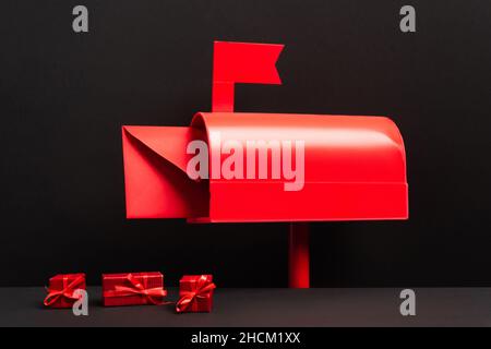 Roter Umschlag in Metallic-Briefkasten neben kleinen Geschenken auf Schwarz Stockfoto