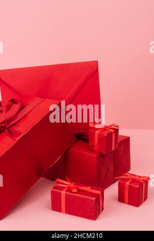 Rot verpackte Geschenkschachteln und Umschlag auf rosa Stockfoto