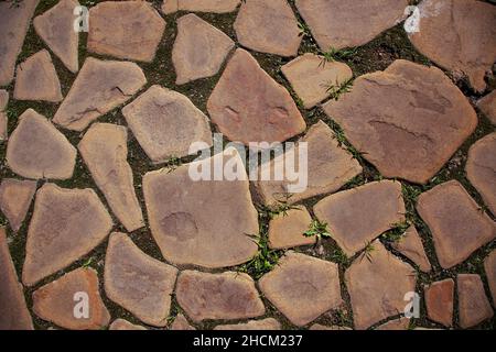 Unstrukturierte geflieste Straße, bestehend aus Pfauen von flachen Steinen in den Boden mit natürlicher Textur mit kleinem Gras zwischen Steinpfauen gelegt. Perfekt nicht Stockfoto