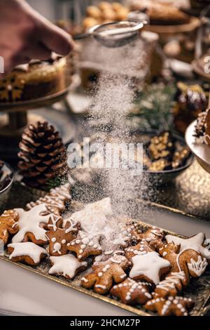 Streut den Puderzucker von Hand auf Lebkuchenkekse. Weihnachtszeit-Cookie-Konzept Stockfoto