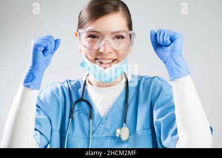 Junge kaukasische Ärztin feiert mit erhobenen Fäusten in der Luft, glückliches medizinisches Personal, nachdem es den Patienten das Leben gerettet hat, lächelt vor Freude Stockfoto