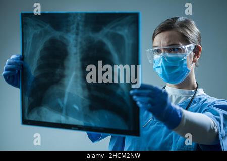 Ärztin im Krankenhaus, die Röntgenfilm des Patienten hält, Radiologin, die das Ergebnis der Radiographie untersucht, Fachärztin für Radiologie, die die Brust des Patienten COVID-19 interpretiert Stockfoto