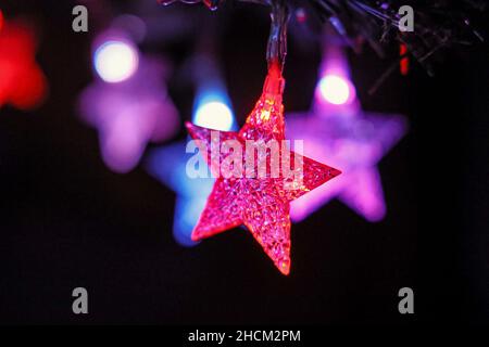 Einfache grafische Aufnahme von sternförmigen bunten Lichtern auf einem Weihnachtsbaum. Nahaufnahme eines roten mit einem Stern im Detail und im Hintergrund blau Stockfoto