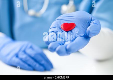 Kardiologe mit schützenden chirurgischen Handschuhen, die das rote Plüschherz in offener Handfläche halten, Gesundheitskonzept, Prävention und Schutz von Patienten Stockfoto