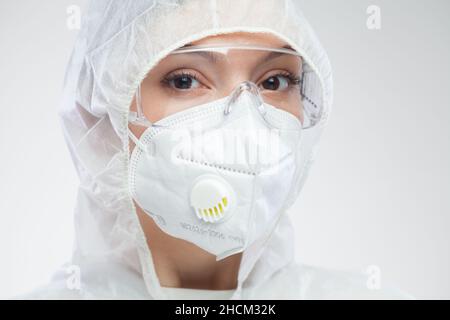 Kopfaufnahme Porträt der schönen kaukasischen jungen medizinischen Arbeiterin, Tragen Schutzbrille, Overalls, N95 Gesichtsmaske, Blick in die Kamera, isoliert Stockfoto