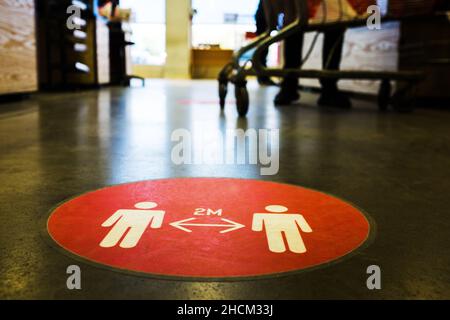 Auf dem Boden an der europäischen Supermarktkasse aufgedrucktes rotes Kreis-Symbol, das die Menschen darauf hinweist, 2 Meter Abstand voneinander zu halten Stockfoto