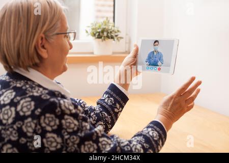 E-Arzt berät ältere ältere Rentnerin zu Hause, digitaler Online-Videoanruf über das Tablet mit Hilfe der On-Demand-App für die Fernhilfe Stockfoto