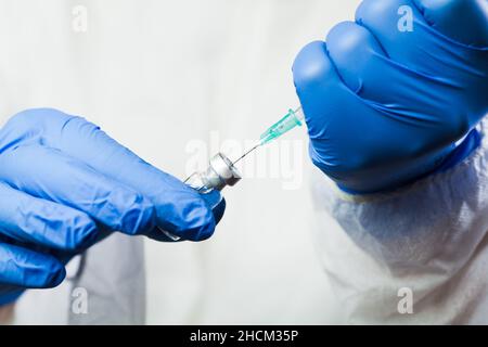 Nahaufnahme der Hände des Arztes in Handschuhen, die die Spritze mit einer Nadel halten, die die Impfstoffdosis abgibt, Coronavirus-Jab gegen die neue COVID-19-Variante Stockfoto