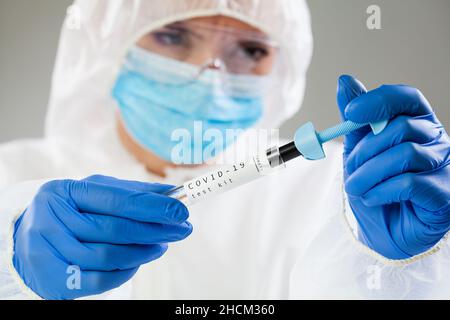 Weibliche medizinische Mitarbeiterin trägt weißen Schutzanzug, Gesichtsmaske und Handschuhe, hält COVID-19 Test-Kit Ausrüstung, Labortechniker Sammlung Patient Stockfoto