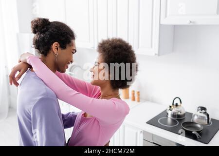 Seitenansicht einer afroamerikanischen Frau, die einen jungen Mann in der Küche umarmt Stockfoto