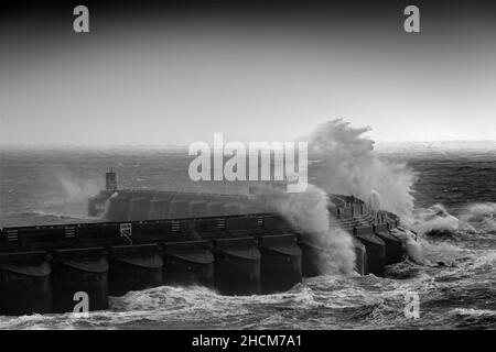 Ein Paar, das im Sturm auf dem Yachthafen herumläuft und Wellen um sie herum krachen Stockfoto