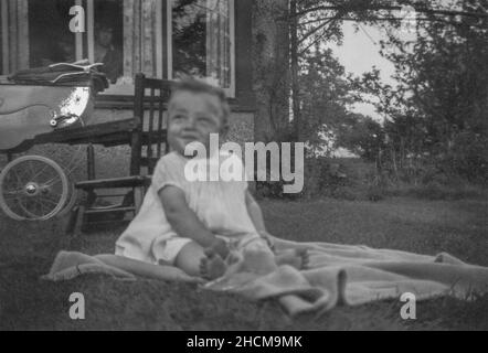 Junger kaukasischer Junge, der draußen auf einer Decke im Garten sitzt 1952 Stockfoto