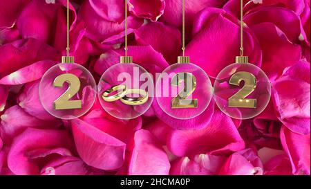 goldene Eheringe in transparenter Glaskugel mit 2022 Ziffern und leuchtendem rosa Rosenblatt-Hintergrund Stockfoto
