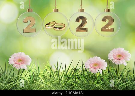 goldene Eheringe in durchsichtiger Glaskugel mit 2022 Ziffern und schönem rosa gerbera grünem Gras Hintergrund Stockfoto