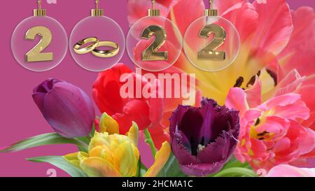 goldene Eheringe in durchsichtiger Glaskugel mit 2022 Ziffern und einem bunten Frühlingsstrauß im Hintergrund Stockfoto