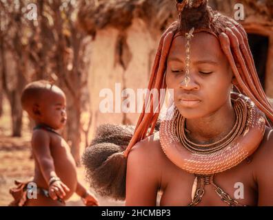 Eine Afrikanerin, die mit ihrem kleinen Kind im ländlichen Namibia traditionellen Himba-Tribal-Schmuck und Frisur trägt. Stockfoto