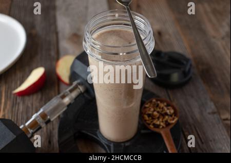 Fitness-Frühstück Shake mit Molkenproteinpulver, hausgemachtem Müsli und frischem Obst. Serviert in einem Shaker auf einem Tisch mit Hantel Stockfoto