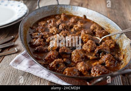 Rustikales Hackfleischgericht mit Fleischbällchen in einer zarten braunen Pilzsauce. Serviert in einer altmodischen Bratpfanne auf einem Holztisch Stockfoto