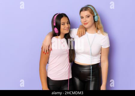 Zwei fröhliche junge Frauen Mädchen Freunde in legerer Kleidung tragen Kopfhörer Musik über lila Hintergrund hören Stockfoto